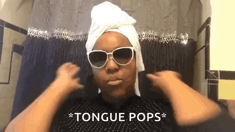 a woman with a towel wrapped around her head is wearing sunglasses and a tongue pops sign .