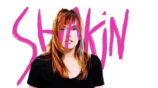 a woman with red hair stands in front of a sign that says shakin