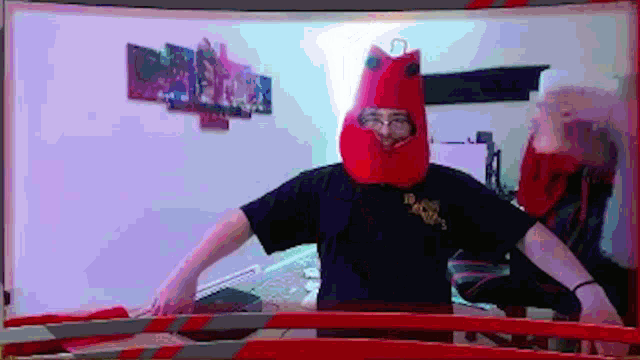 a man wearing a red hat and a black shirt is standing in front of a computer screen .