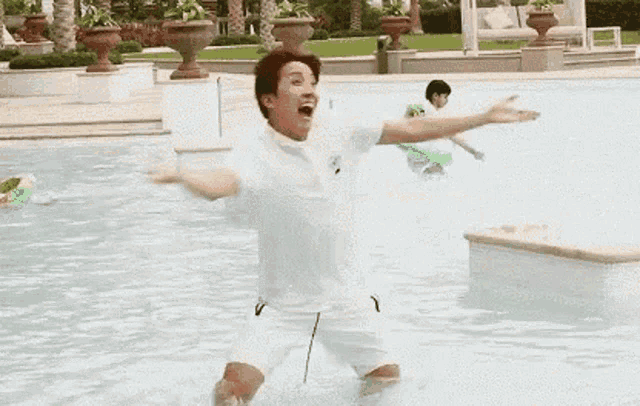 a man in a white shirt is jumping into a swimming pool .