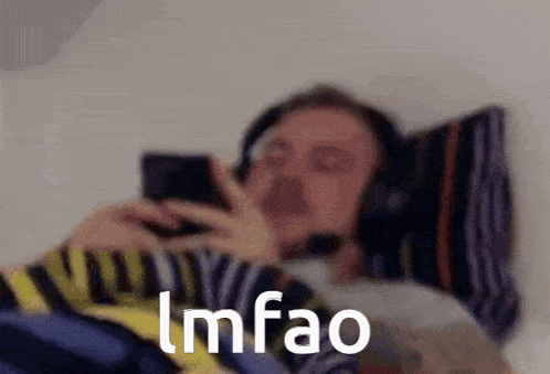 a man wearing headphones is laying in bed looking at his phone .