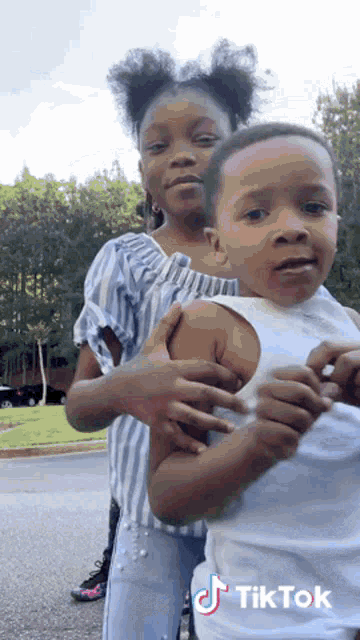 a little girl is holding a little boy in her arms with a tiktok logo on the bottom right