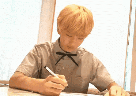 a young man with blonde hair is writing on a piece of paper with a marker .
