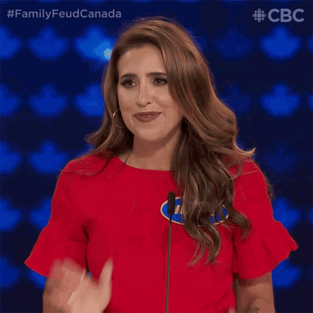 a woman in a red shirt is applauding in front of a microphone with the words family feud canada behind her