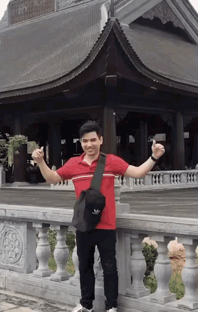 a man wearing a red shirt and a black adidas bag