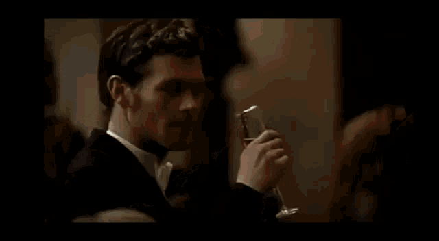 a man in a tuxedo is drinking a glass of wine .