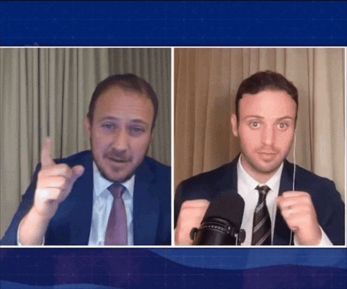 a man in a suit and tie talks into a microphone while another man looks on