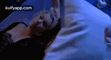 a woman is laying in a bed with a blue blanket and a person holding her head .