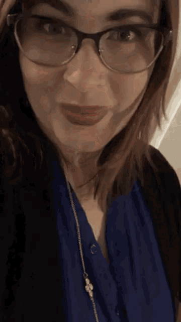 a woman wearing glasses and a blue shirt is taking a selfie