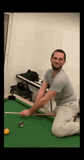 a man is kneeling on a pool table with a pool cue in his hand