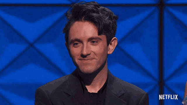 a man in a suit says thank you in front of a blue background