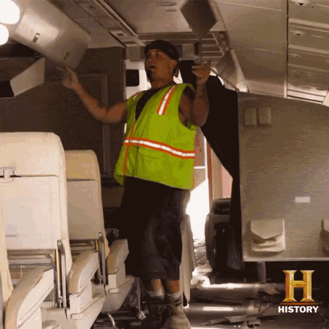 a man in a green vest is standing in an airplane with the letter h on the bottom
