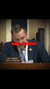 a man in a suit and tie is speaking into a microphone with the name mr. chew above him