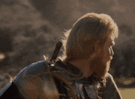 a man with long blonde hair and a beard is standing in front of a mountain