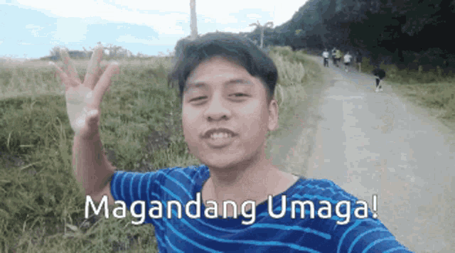 a man in a blue and white striped shirt is waving in front of a sign that says maganda