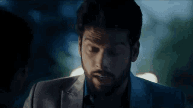 a man with a beard is wearing a suit and looking at the camera with a surprised look on his face .
