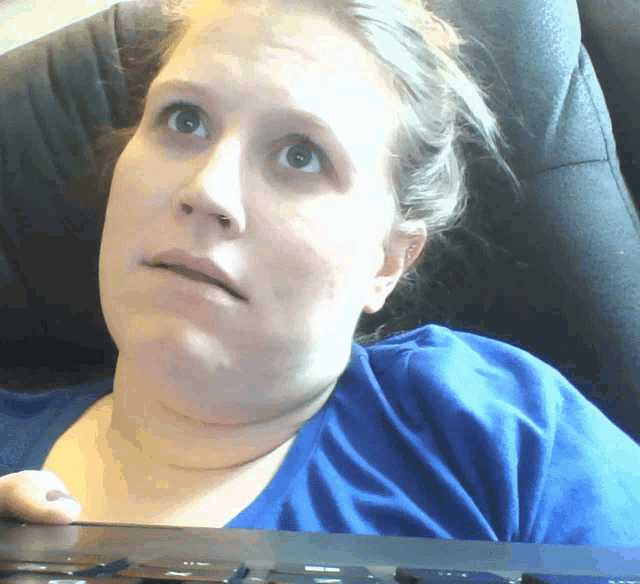 a woman in a blue shirt is sitting in a chair looking at the camera