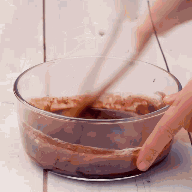 a person is stirring a brown liquid in a glass bowl