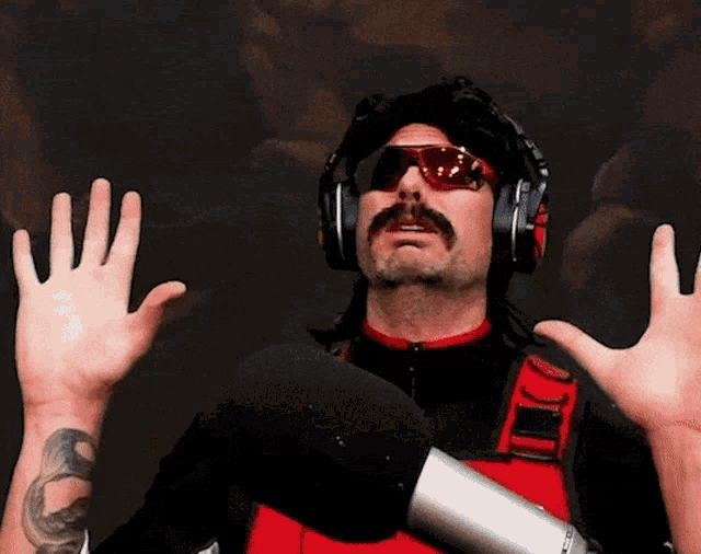 a man wearing headphones and sunglasses holds up his hands in the air