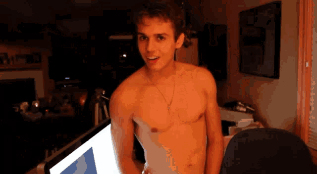 a shirtless young man stands in front of a computer monitor
