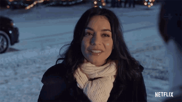 a woman wearing a scarf and a coat is smiling in the snow .