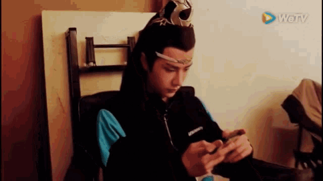a young man is sitting in a chair looking at his phone .