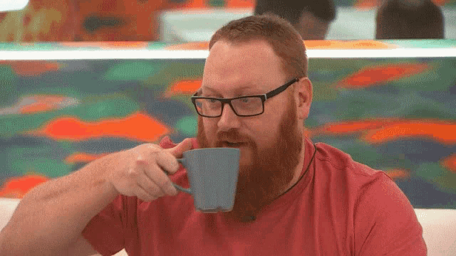 a man with a beard and glasses is drinking from a blue mug .
