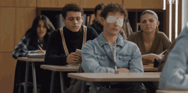 a man with an eye patch sits in a classroom with other students