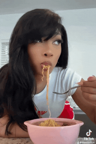 a woman is eating noodles from a pink bowl with a tiktok watermark on the bottom