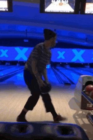 a man is throwing a bowling ball in a bowling alley with a x on the wall behind him