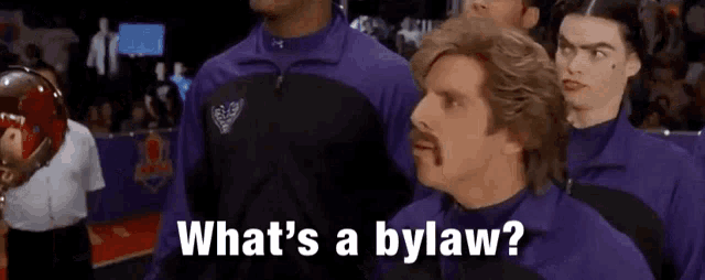 a man with a mustache is standing next to a group of men and says what 's a bylaw .