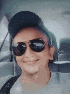 a man wearing sunglasses and a hat is smiling in the back seat of a car