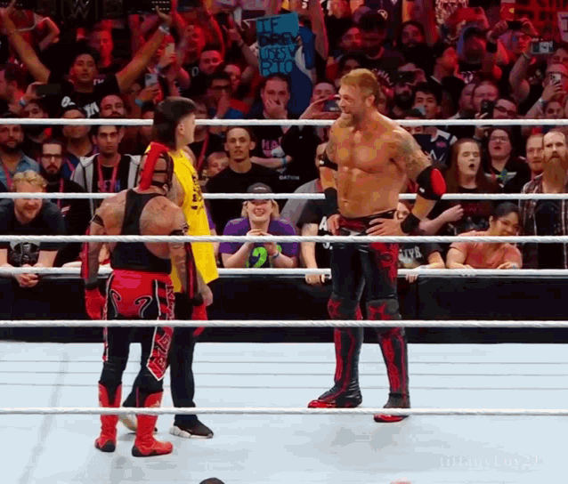 a man in a yellow shirt with the number 2 on it stands in a wrestling ring with two other men