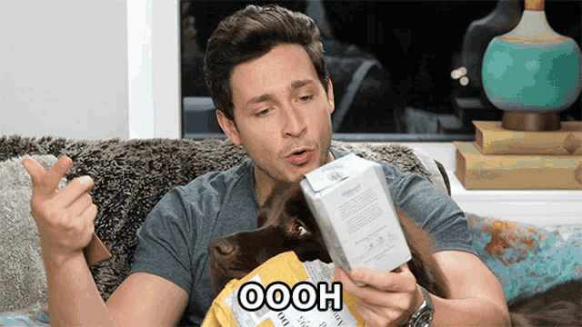 a man sitting on a couch with a dog and a box that says oooh on it