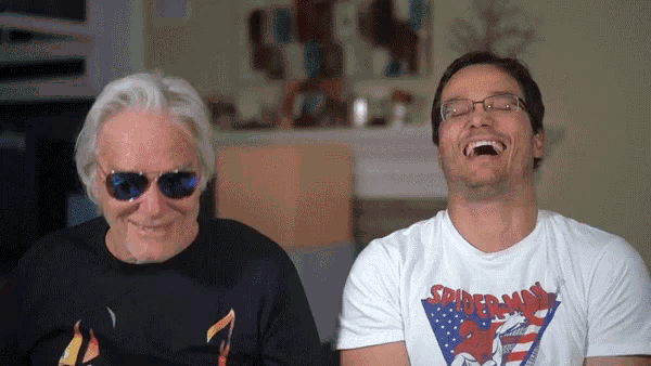 a man wearing a spiderman shirt is laughing next to an older man