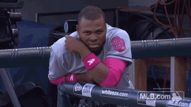 a man in a san diego baseball uniform leans on a fence