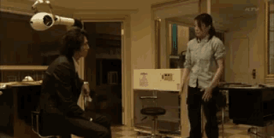 a man in a suit sits on a bar stool talking to a woman in a room with ktv written on the bottom
