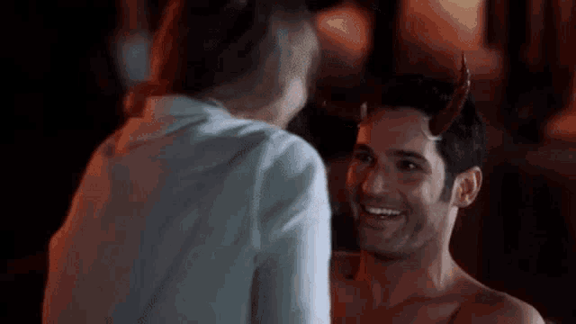 a shirtless man with horns on his head is smiling at a woman .
