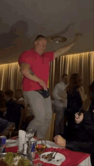 a man in a red shirt is dancing in a restaurant while another man sits at a table