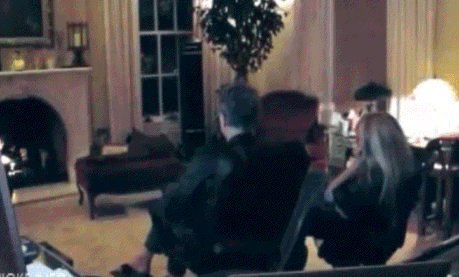 a group of people are sitting in a living room with a fireplace in the background