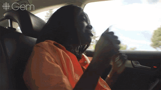 a woman in an orange shirt is sitting in the back seat of a car with the word gem on the bottom left