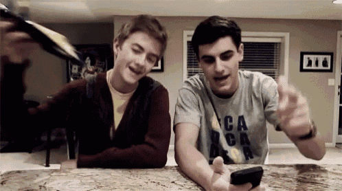 two young men are sitting at a table and one has a shirt that says " ca " on it