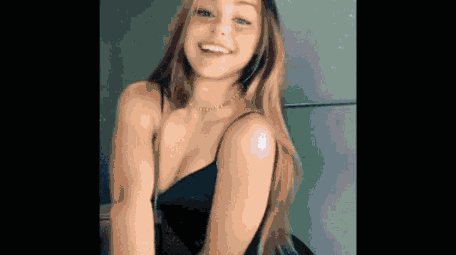 a young woman in a black tank top and necklace is smiling and dancing .