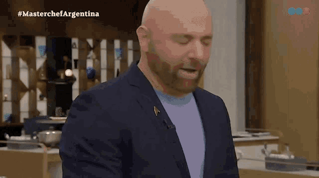 a bald man with a beard is standing in front of a television screen that says masterchef argentina