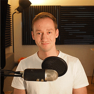 a man in a white shirt is standing in front of a microphone and smiling