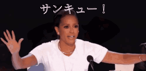 a woman in a white shirt is sitting in front of a microphone with her arms outstretched in front of a crowd .