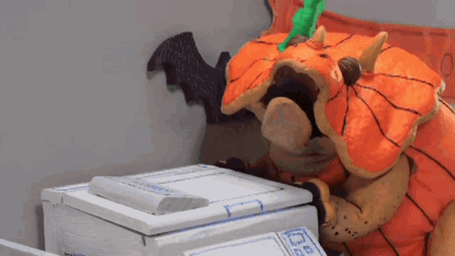 a stuffed animal in an orange pumpkin costume is looking at a box with a sticker on it