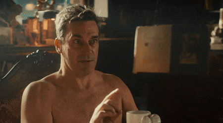 a shirtless man sits in a chair with a cup of coffee
