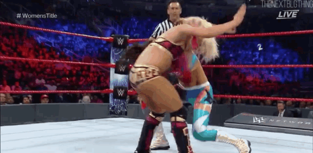 two women are wrestling in a wrestling ring with a referee watching