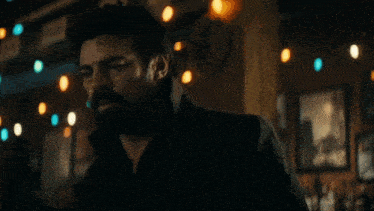a man with a beard is standing in a dark room with lights on the ceiling .
